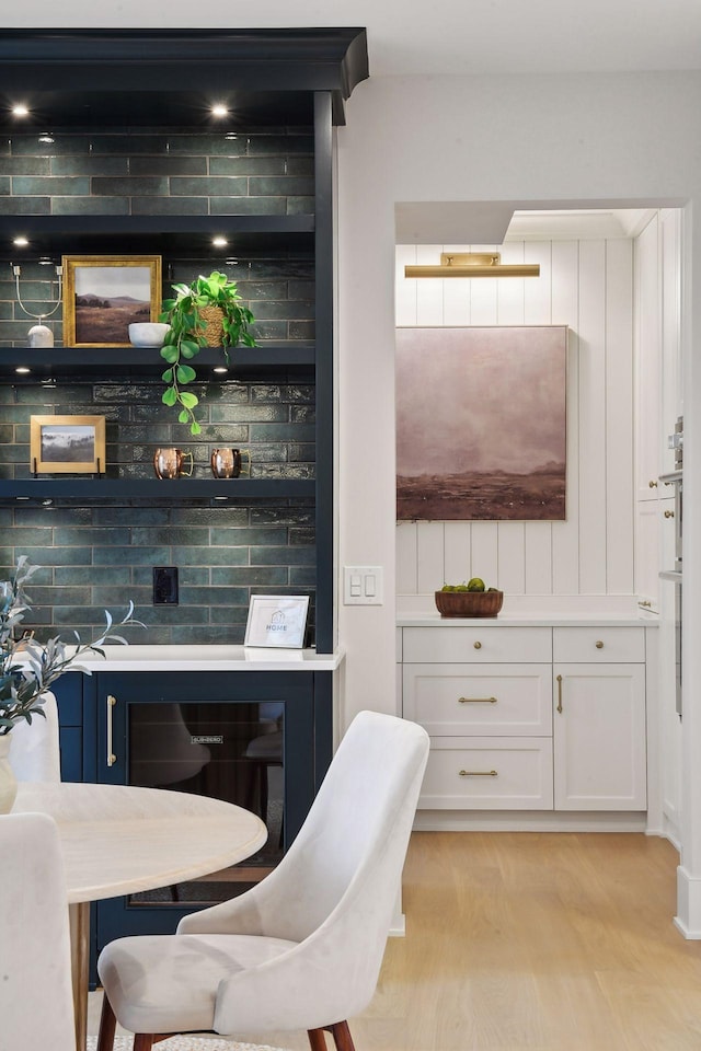 bar featuring white cabinets, light hardwood / wood-style flooring, and backsplash