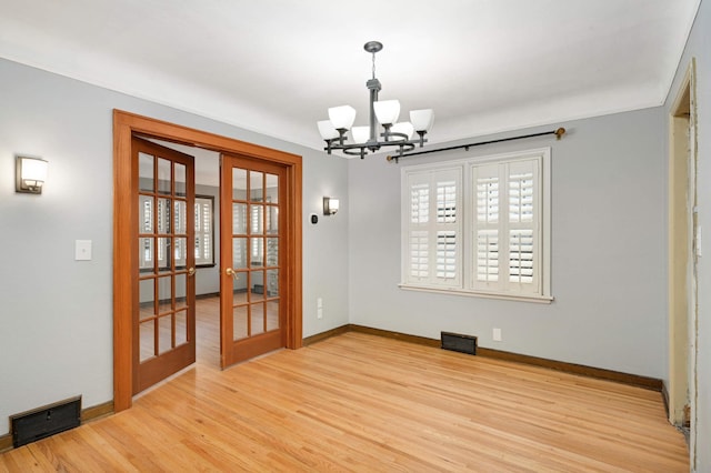 unfurnished dining area with a notable chandelier, light hardwood / wood-style floors, and french doors