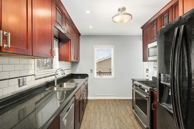 kitchen featuring appliances with stainless steel finishes, sink, dark stone countertops, backsplash, and light hardwood / wood-style floors