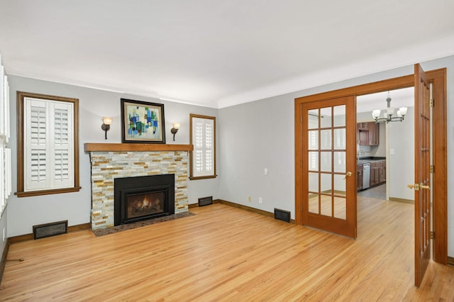 living room with a stone fireplace, light hardwood / wood-style flooring, and a notable chandelier