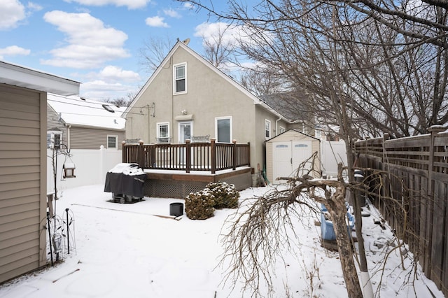 snow covered back of property with a shed and a wooden deck