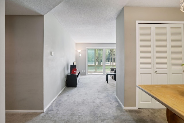 corridor with light carpet and a textured ceiling