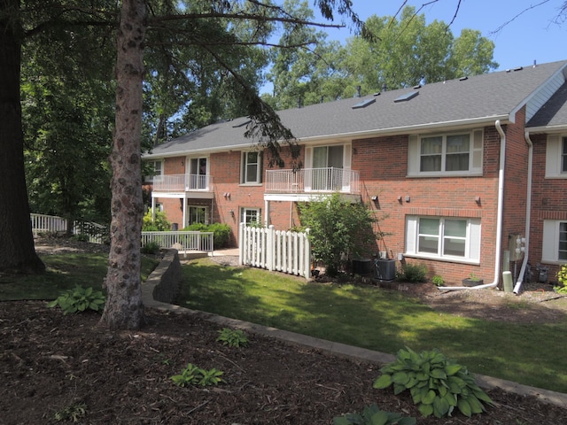 rear view of property featuring a lawn, a balcony, and cooling unit