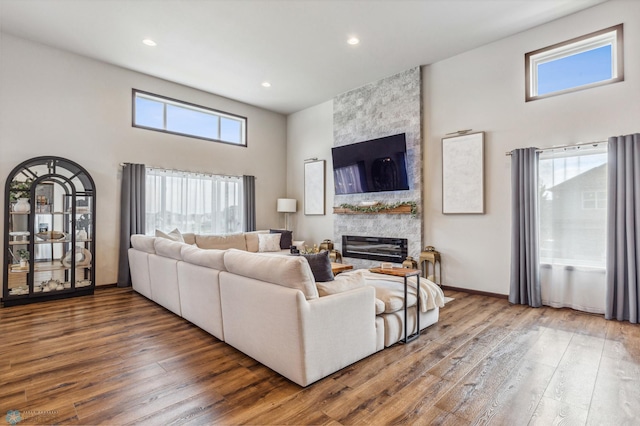 living room with a fireplace, a towering ceiling, a healthy amount of sunlight, and wood-type flooring