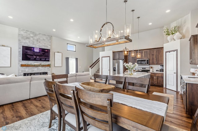 dining area with a stone fireplace, dark hardwood / wood-style flooring, a towering ceiling, and sink