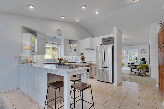 kitchen featuring stainless steel appliances, wall chimney range hood, vaulted ceiling, white cabinets, and kitchen peninsula