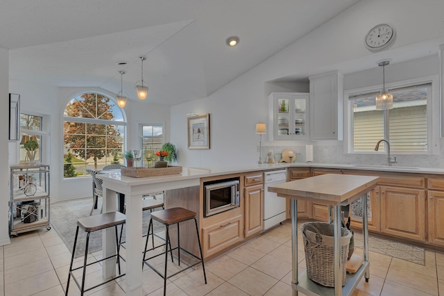 kitchen featuring sink, dishwasher, stainless steel microwave, light brown cabinetry, and vaulted ceiling