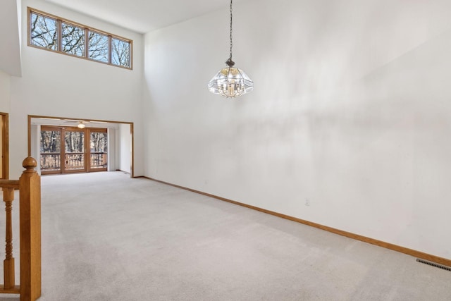 interior space featuring a healthy amount of sunlight, light colored carpet, a towering ceiling, and a chandelier