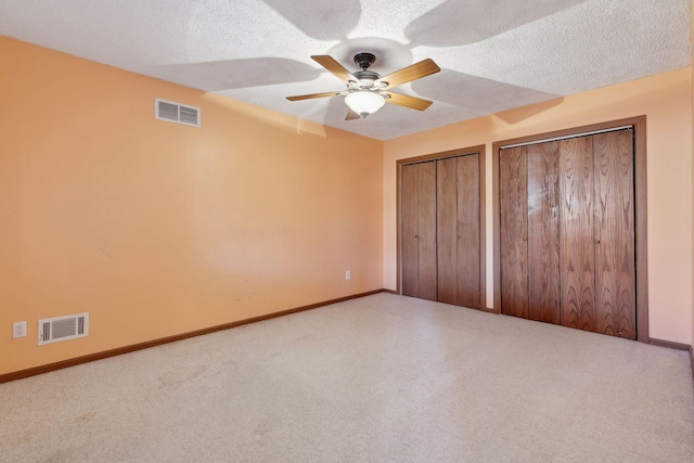 unfurnished bedroom featuring carpet flooring, two closets, ceiling fan, and a textured ceiling