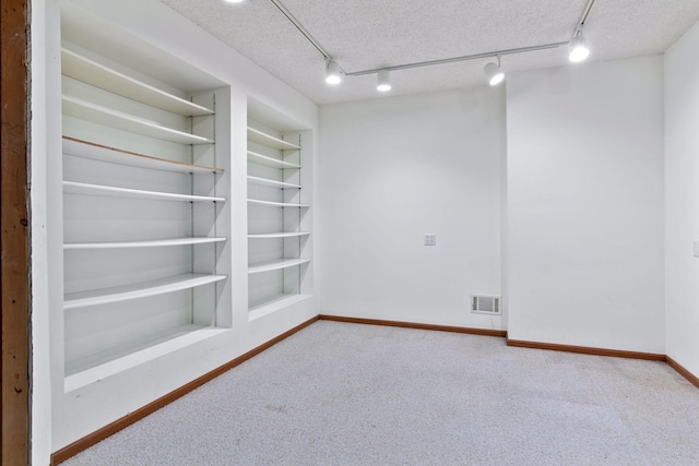 carpeted spare room with rail lighting, a textured ceiling, and built in shelves