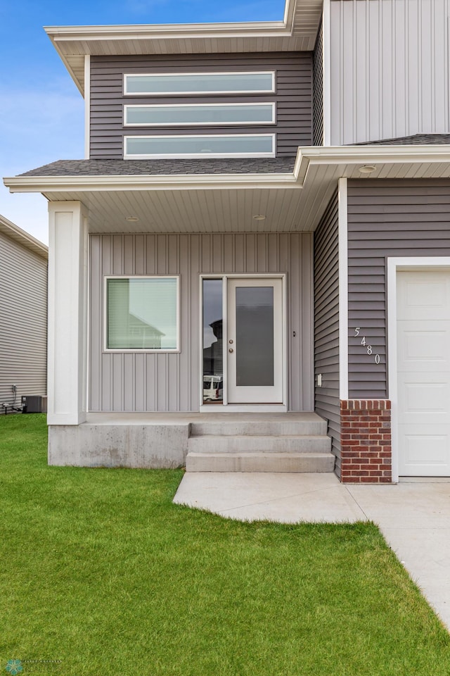 view of exterior entry with a garage, central AC unit, and a lawn