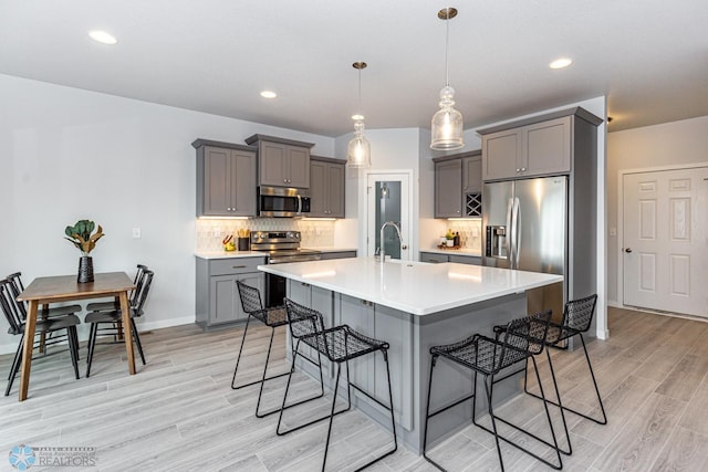 kitchen featuring light hardwood / wood-style floors, appliances with stainless steel finishes, a breakfast bar area, gray cabinets, and pendant lighting