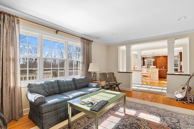 living area featuring crown molding, baseboards, decorative columns, and light wood-style floors