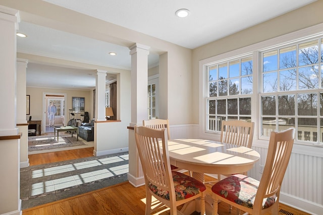 dining room with a wainscoted wall, crown molding, decorative columns, recessed lighting, and wood finished floors