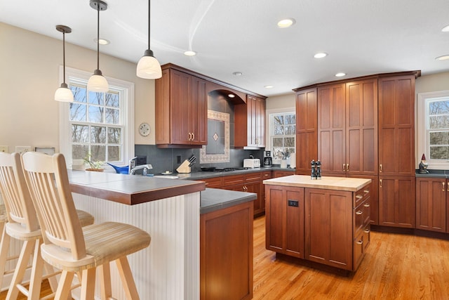 kitchen featuring light wood-style flooring, hanging light fixtures, a center island, dark countertops, and plenty of natural light