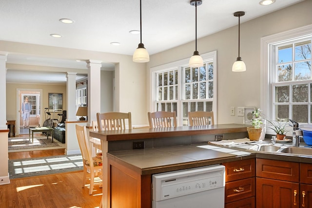 kitchen featuring light wood-type flooring, white dishwasher, decorative columns, and decorative light fixtures