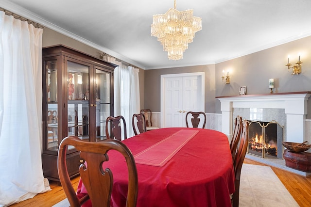 dining room featuring a tiled fireplace, ornamental molding, light wood-type flooring, and a chandelier