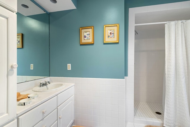 bathroom with a wainscoted wall, a shower stall, tile walls, and vanity