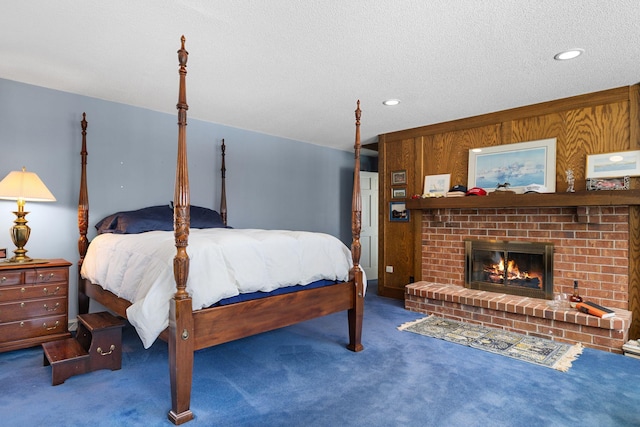 bedroom featuring a textured ceiling, dark carpet, wood walls, and a fireplace