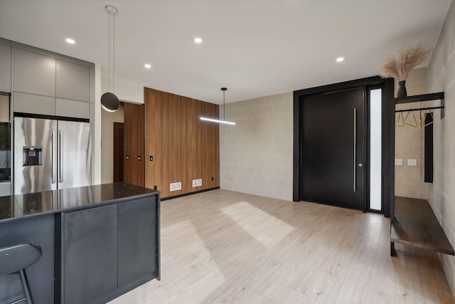 kitchen featuring light hardwood / wood-style flooring, dark stone counters, pendant lighting, and stainless steel fridge with ice dispenser