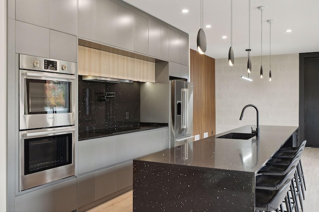 kitchen featuring light hardwood / wood-style flooring, dark stone countertops, sink, pendant lighting, and appliances with stainless steel finishes