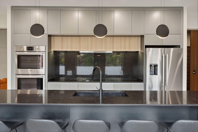 kitchen with dark stone counters, sink, a breakfast bar, gray cabinets, and appliances with stainless steel finishes