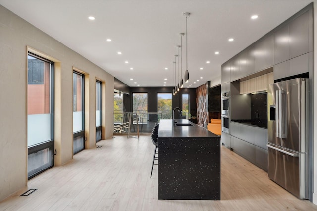 kitchen with a large island, a kitchen bar, light wood-type flooring, stainless steel appliances, and decorative light fixtures