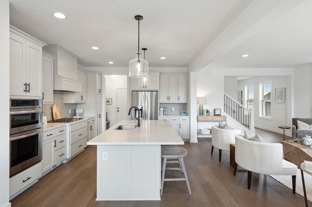 kitchen featuring sink, an island with sink, stainless steel appliances, pendant lighting, and dark hardwood / wood-style floors