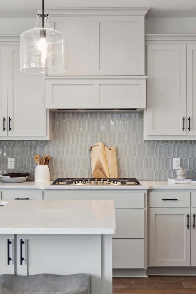 kitchen with tasteful backsplash, light stone countertops, stainless steel gas cooktop, hanging light fixtures, and dark hardwood / wood-style floors