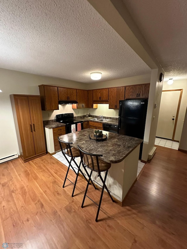 kitchen featuring a kitchen bar, black appliances, light hardwood / wood-style floors, a textured ceiling, and a kitchen island