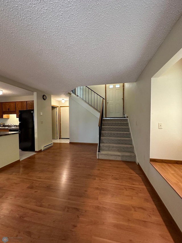 unfurnished living room with light hardwood / wood-style floors, a textured ceiling, and baseboard heating