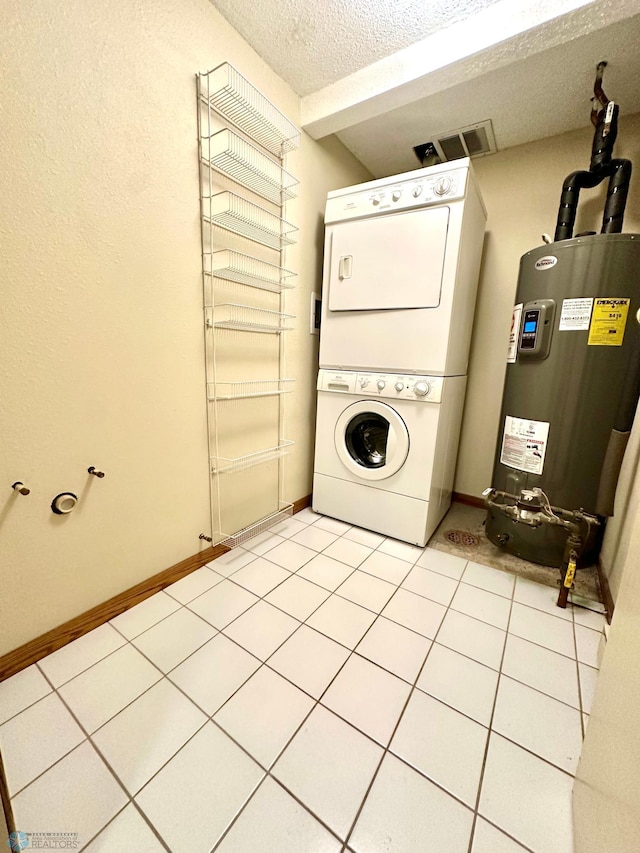 washroom with light tile patterned floors, electric water heater, a textured ceiling, and stacked washing maching and dryer