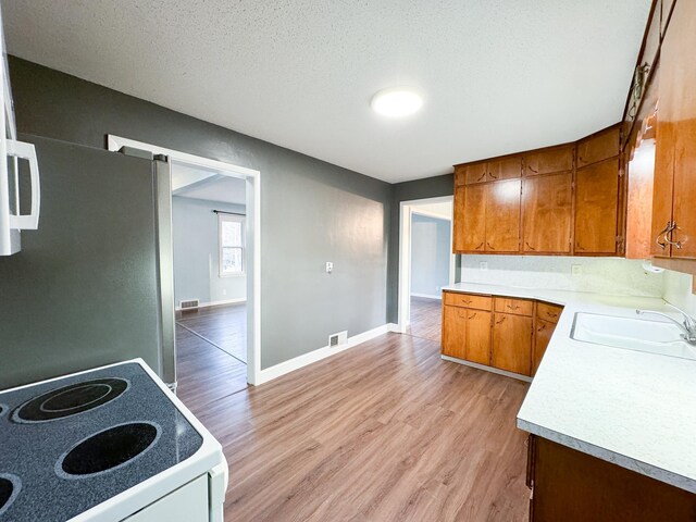 kitchen with sink, a textured ceiling, stainless steel fridge, light hardwood / wood-style floors, and stove