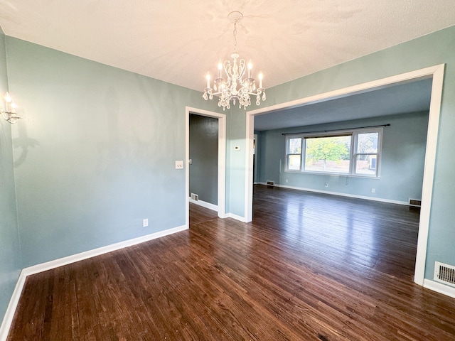 unfurnished room with a textured ceiling, an inviting chandelier, and dark hardwood / wood-style floors