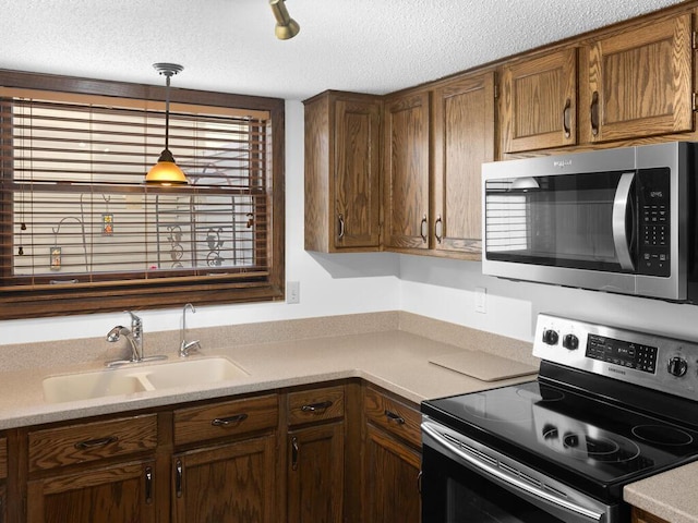 kitchen with pendant lighting, a textured ceiling, stainless steel appliances, and sink