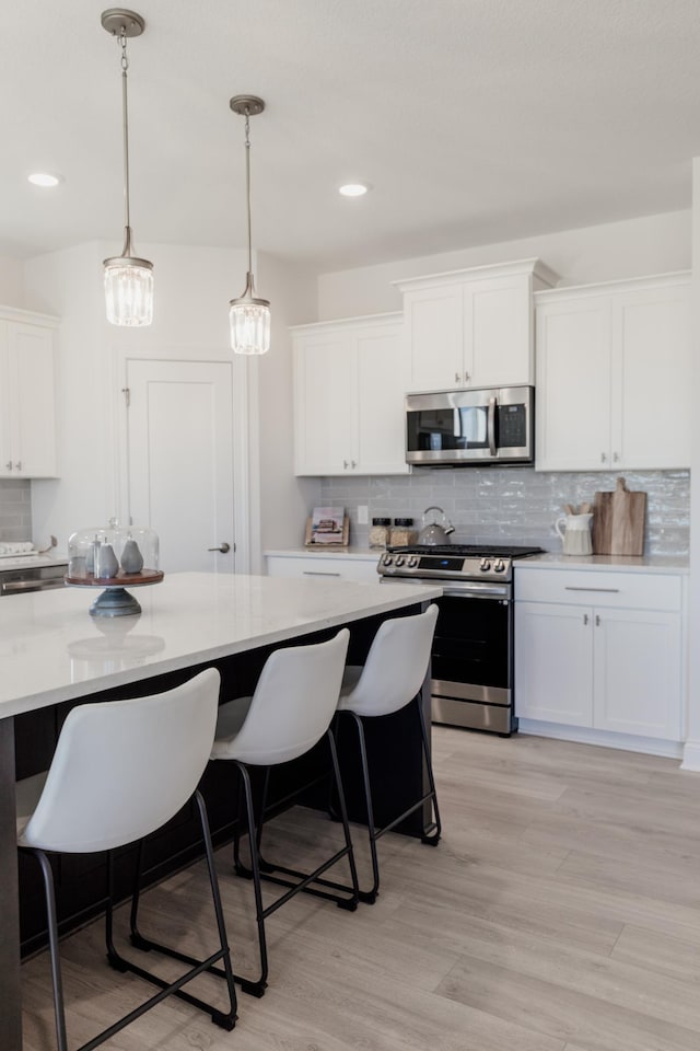 kitchen featuring white cabinetry, light wood-type flooring, stainless steel appliances, and pendant lighting