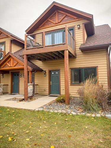 rear view of property featuring a balcony, a yard, and a patio