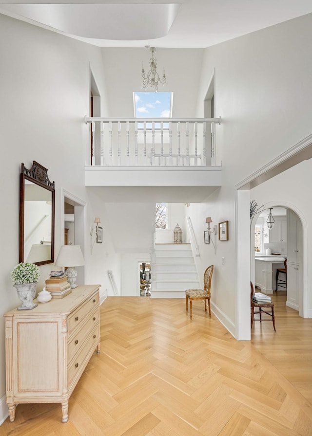 interior space with arched walkways, a notable chandelier, stairway, a high ceiling, and baseboards