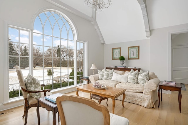 living area with a wealth of natural light, light wood-type flooring, a towering ceiling, and visible vents