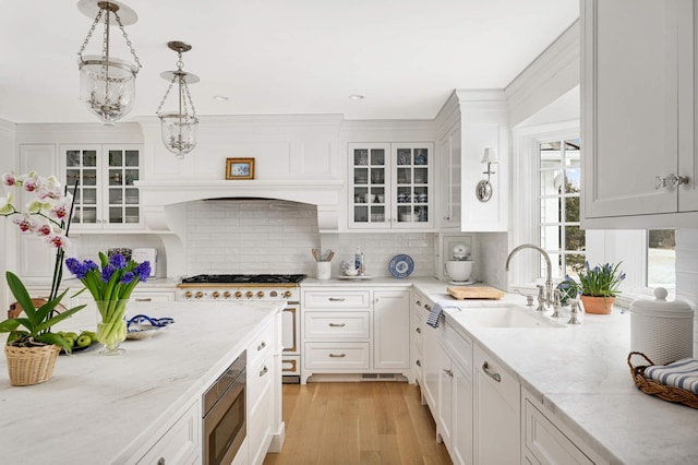 kitchen featuring white cabinets, a sink, stainless steel appliances, light wood-type flooring, and backsplash