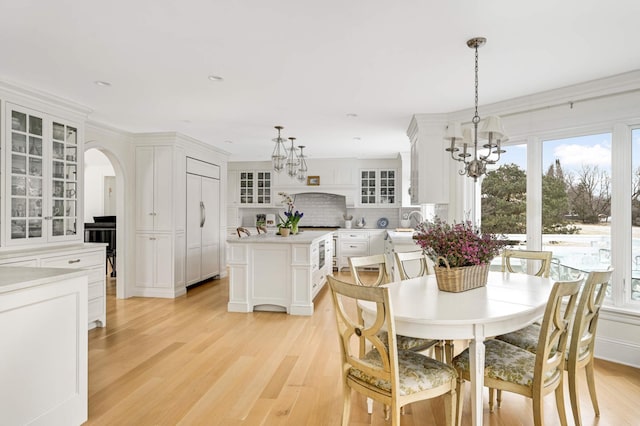 dining area with light wood-style floors, arched walkways, a wealth of natural light, and a notable chandelier