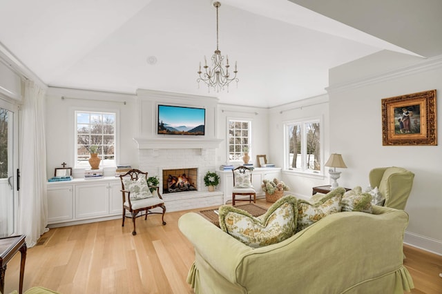 living area with baseboards, ornamental molding, light wood-style floors, a fireplace, and a notable chandelier