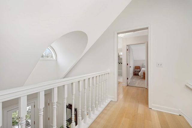 corridor featuring lofted ceiling, light wood-style flooring, and baseboards