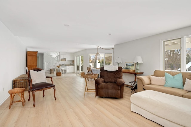 living room featuring light wood-style flooring, baseboards, and stairs