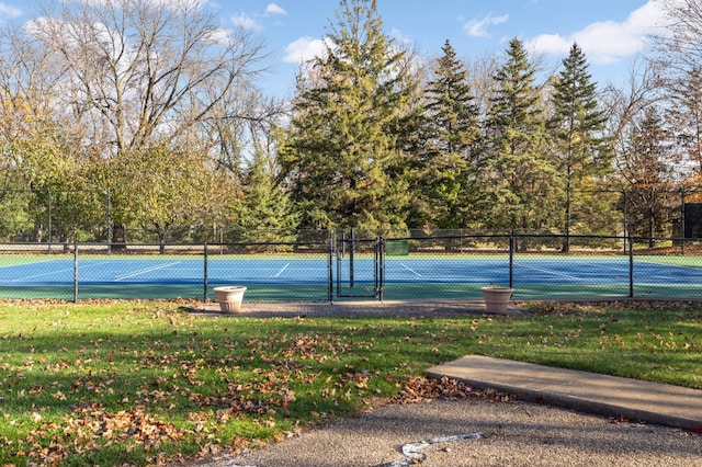 view of tennis court with a yard and fence