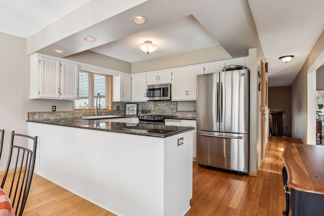 kitchen with kitchen peninsula, stainless steel appliances, sink, light hardwood / wood-style flooring, and white cabinets