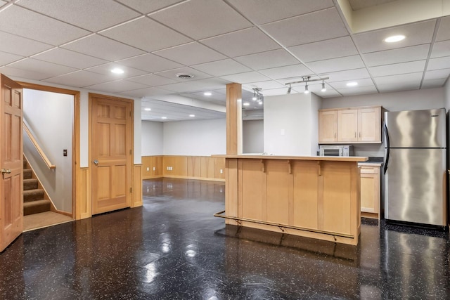 kitchen featuring a kitchen breakfast bar, stainless steel refrigerator, light brown cabinetry, and a drop ceiling