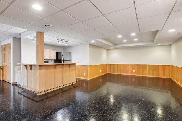 interior space with kitchen peninsula, stainless steel fridge, a kitchen bar, light brown cabinetry, and wooden walls