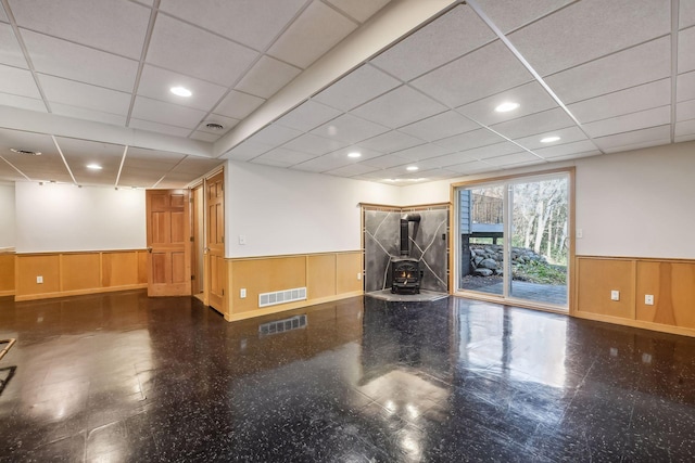 interior space with a paneled ceiling, a wood stove, and wood walls