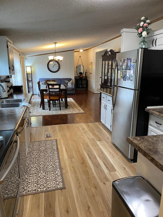 kitchen with appliances with stainless steel finishes, crown molding, white cabinetry, and light wood-type flooring